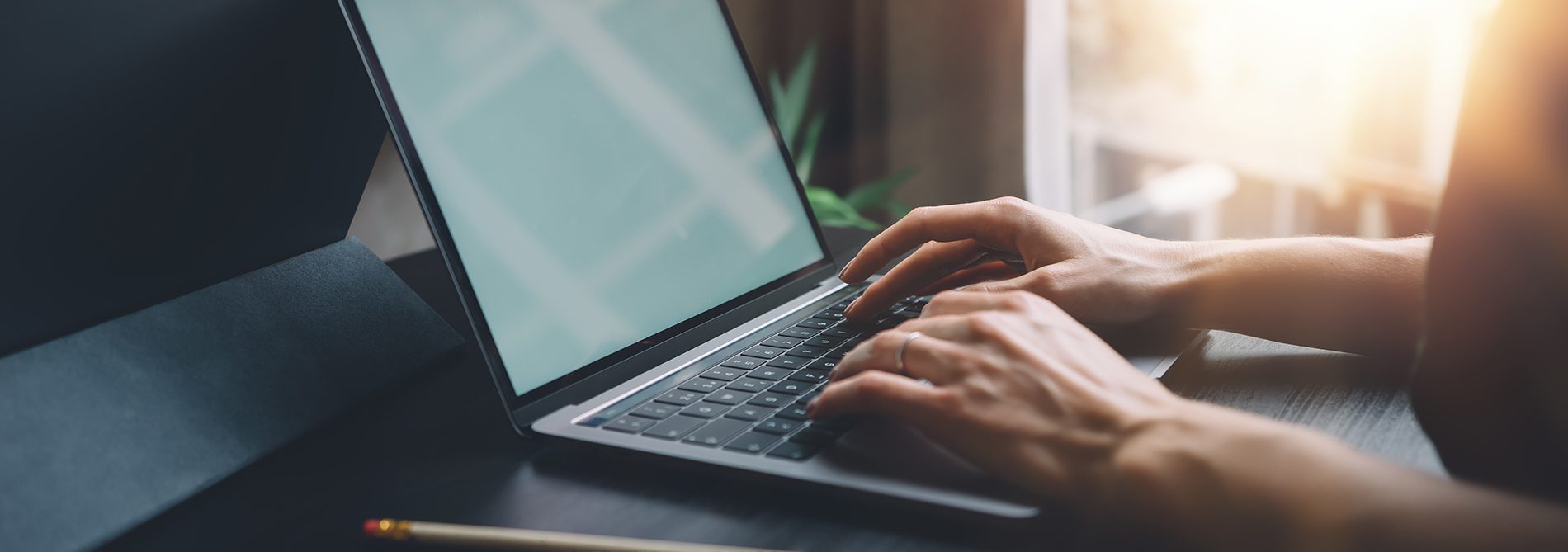 Female hands typing on laptop keyboard at the office. Wide.